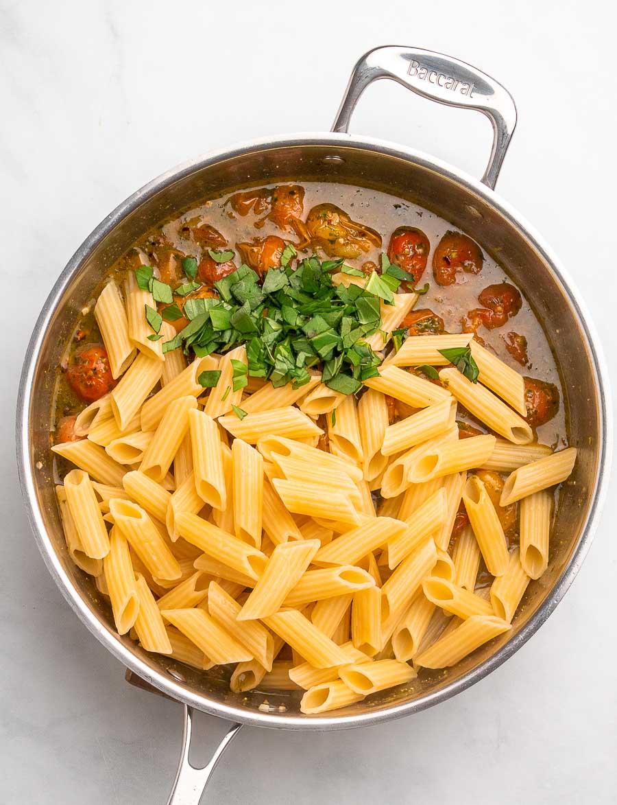 top down shot of the cherry tomato pasta in the skillet after pasta and basil are placed in