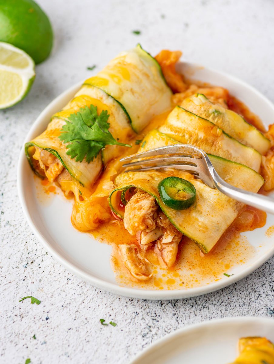 a fork cutting into a piece of chicken zucchini enchiladas