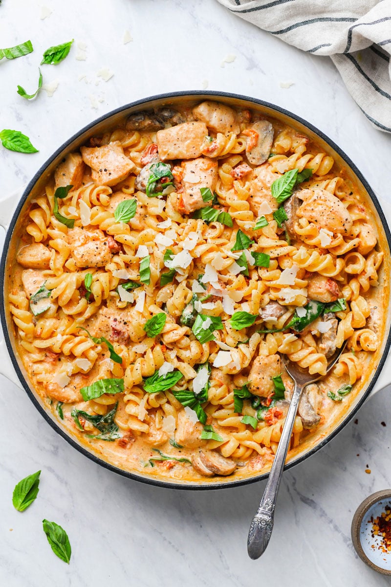 creamy mushroom chicken pasta in a skillet garnished with basil