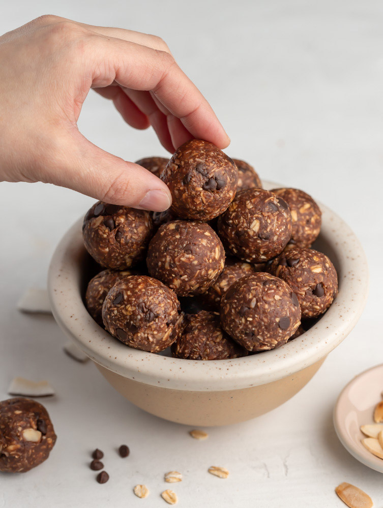 side shot of almond joy energy balls in a bowl with a hand picking up one piece