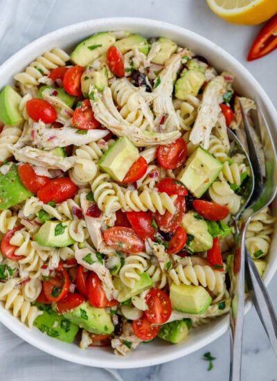 A bowl of avocado chicken pasta salad with a fork and spoon in the bowl.