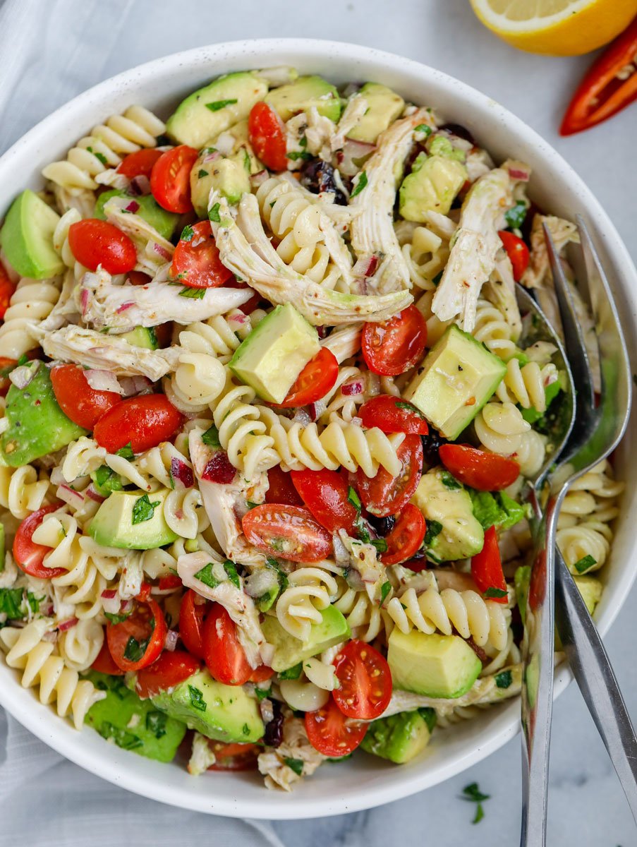 A bowl of avocado chicken pasta salad with a fork and spoon in the bowl.