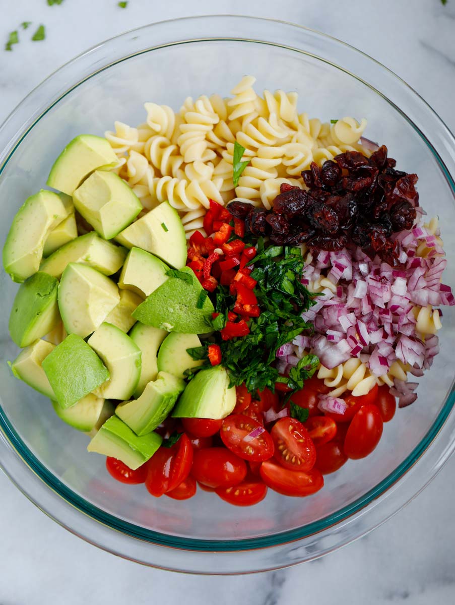 Ingredients for avocado chicken pasta salad chopped and in a bowl together.
