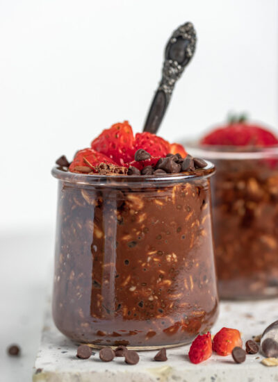 close up shot of chocolate overnight oats in a cup topped with strawberries and spoon inside the cup