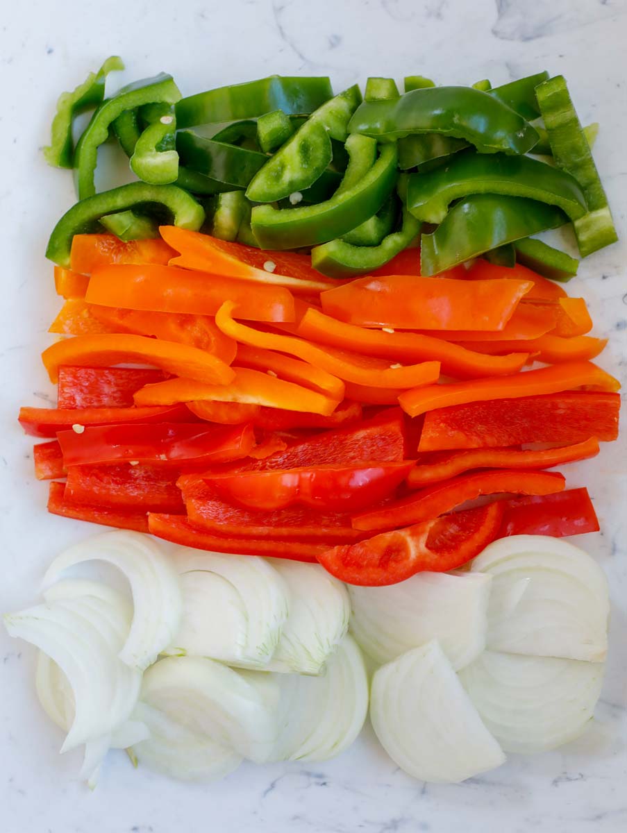 Green bell pepper, red bell pepper, orange bell pepper, and onions cut up.