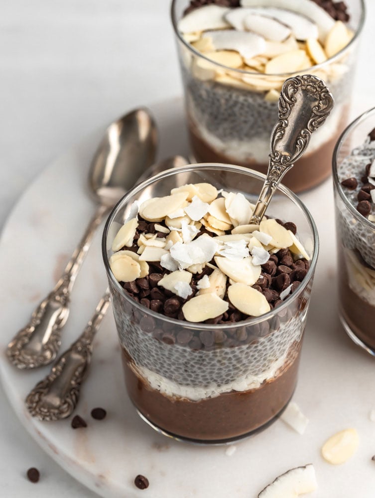 almond joy chia pudding in a cup garnished with some nuts and chocolate chips