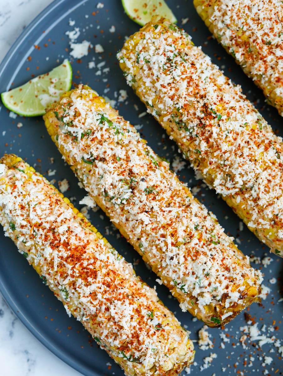 Close up of Mexican street corn on a plate with lots of cheese on top.