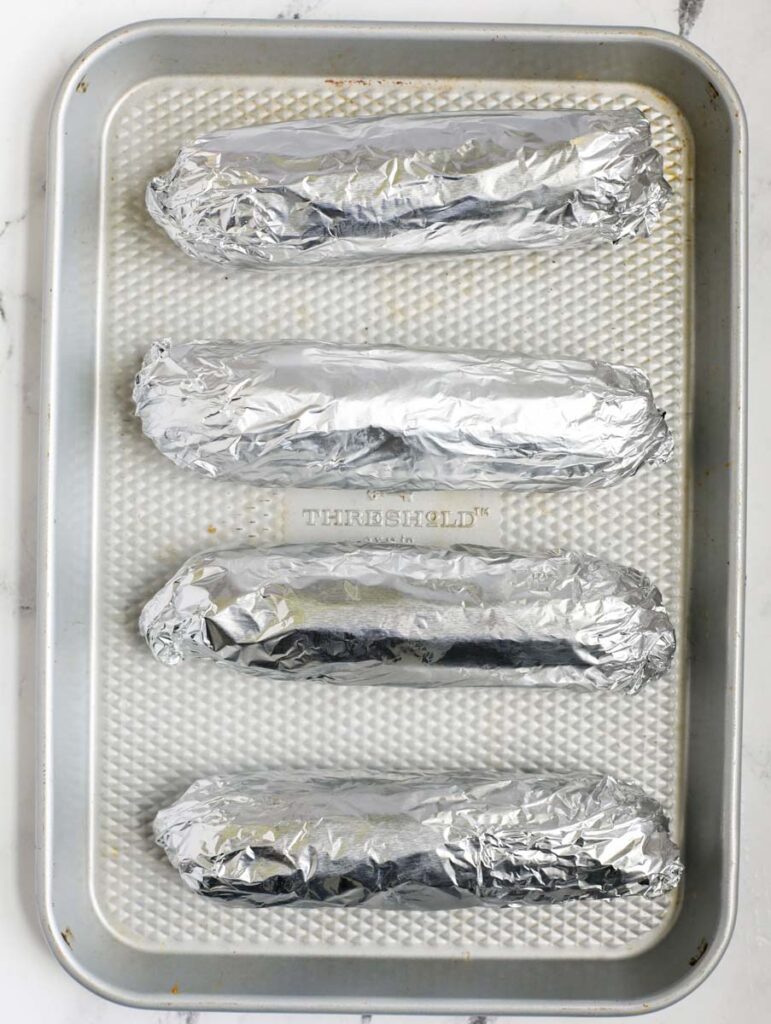 Tin foil wrapped corn on a sheet pan.