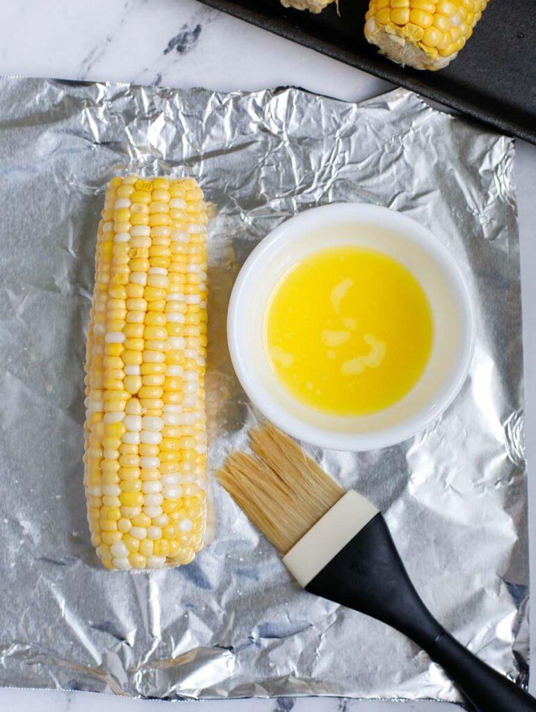 Butter brushed on a corn on the cob on top of tin foil.