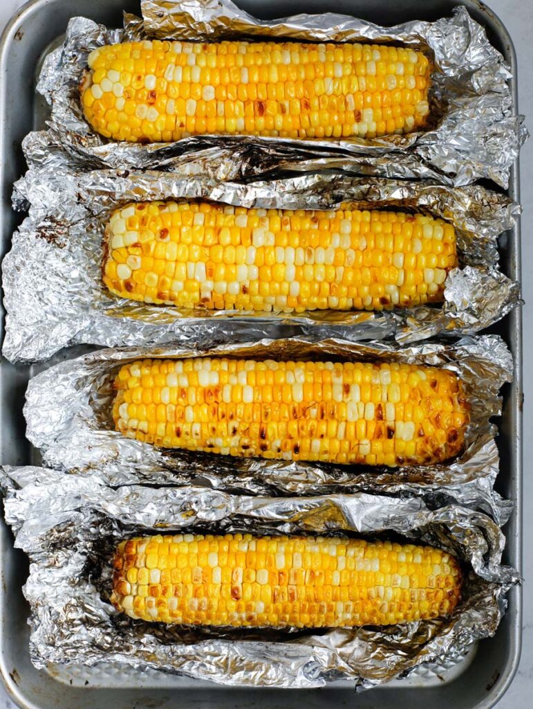 Grilled corn wrapped with tinfoil on a sheet pan.