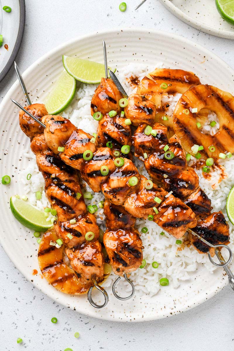 Hawaiian chicken skewers on a plate over rice.