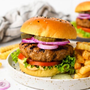 A homemade burger on a plate with toppings and fries.