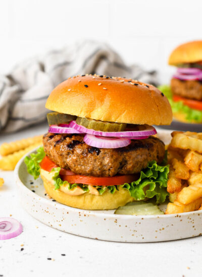 A homemade burger on a plate with toppings and fries.