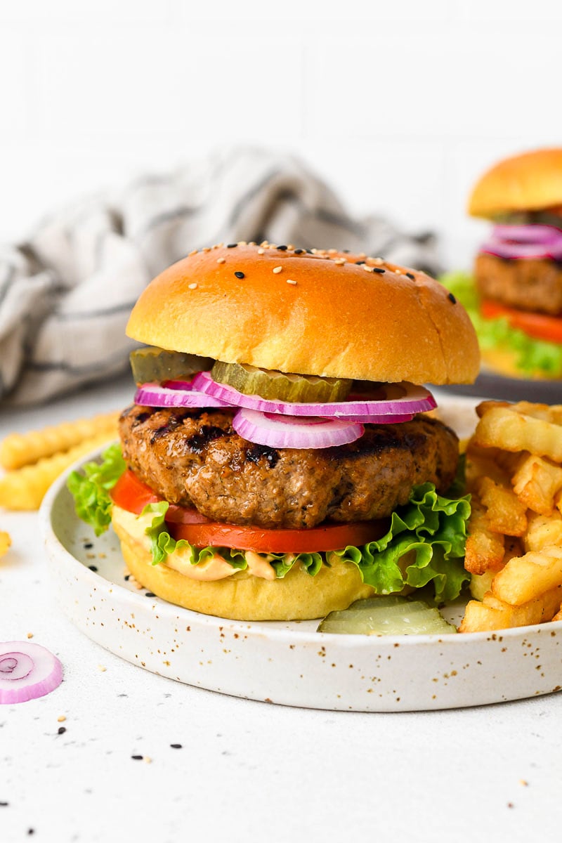 A homemade burger on a plate with toppings and fries.