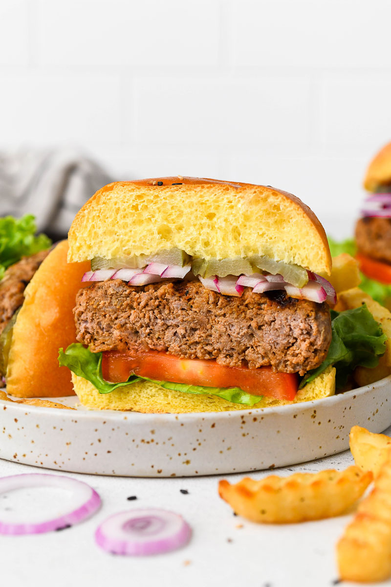 Half of a beef burger on a plate with sides.