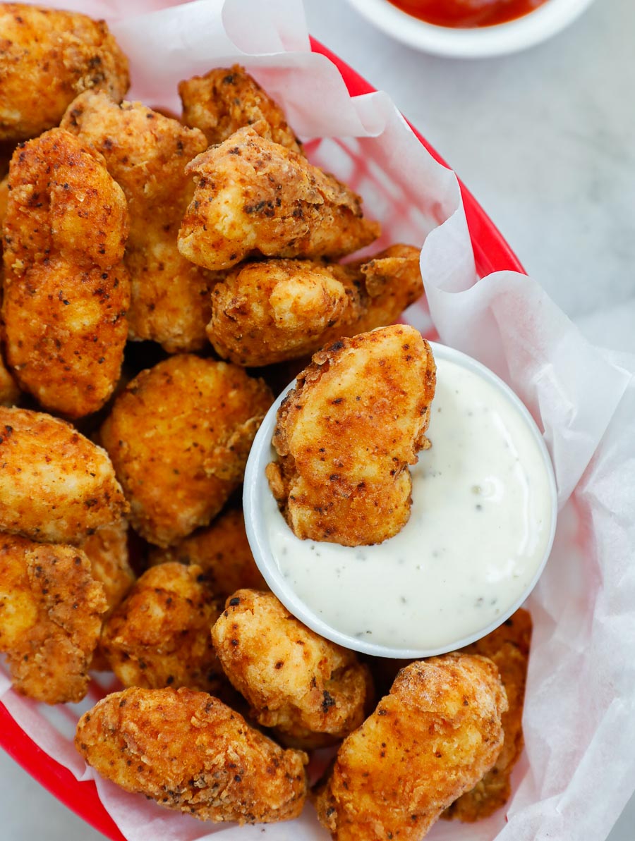 chicken bites in a red basket with a side of ranch and one chicken bite dipped in ranch.