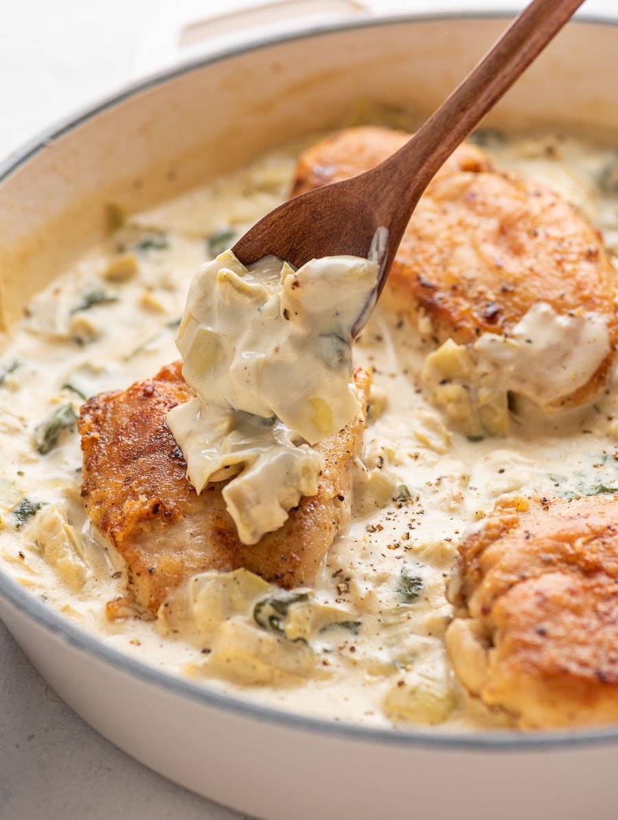 creamy spinach artichoke sauce being placed on top of the chicken