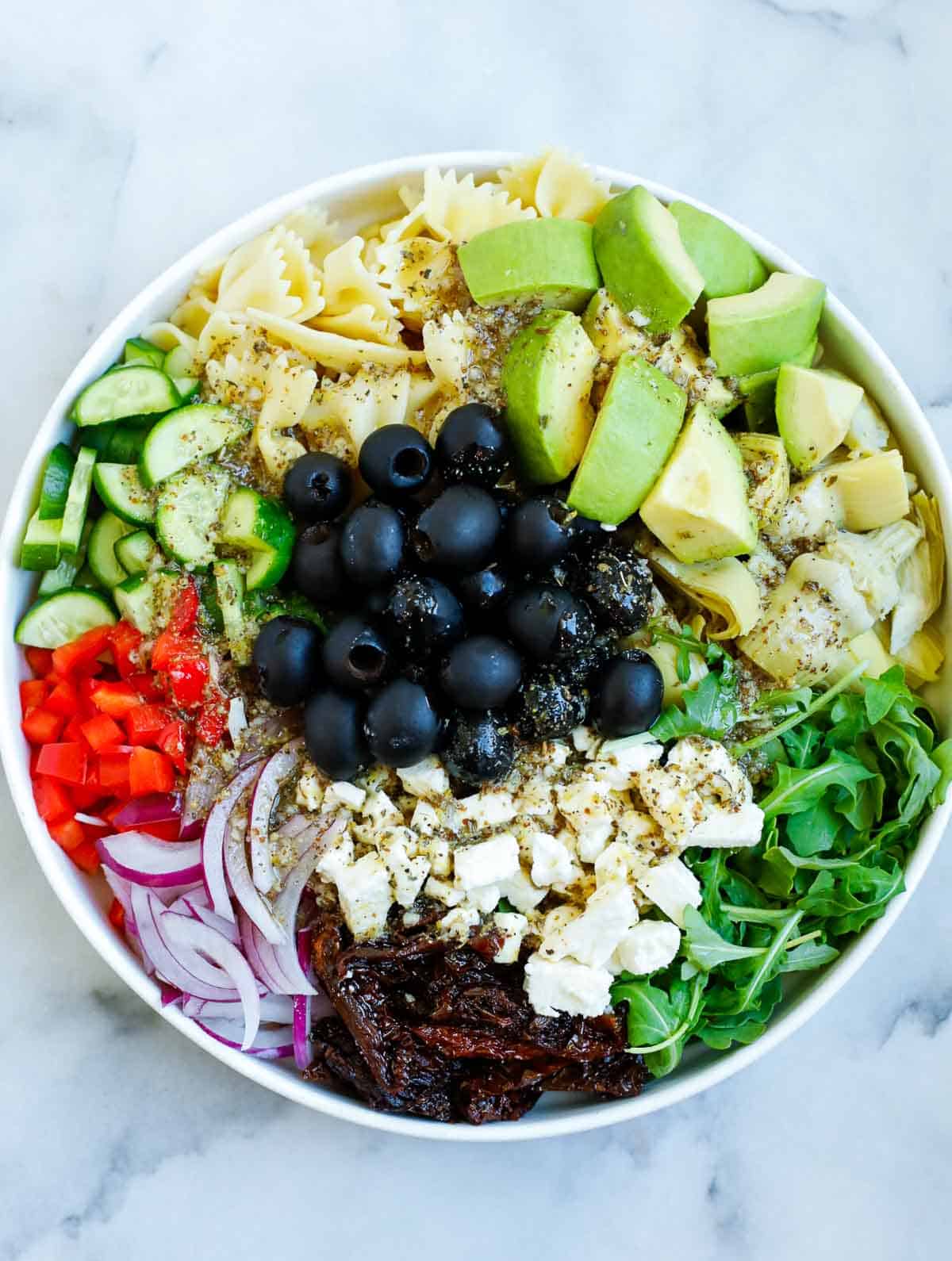 Salad dressing added to a bowl of Mediterranean salad.