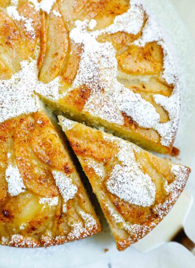 A piece of cake being taken out of the whole pear cake.
