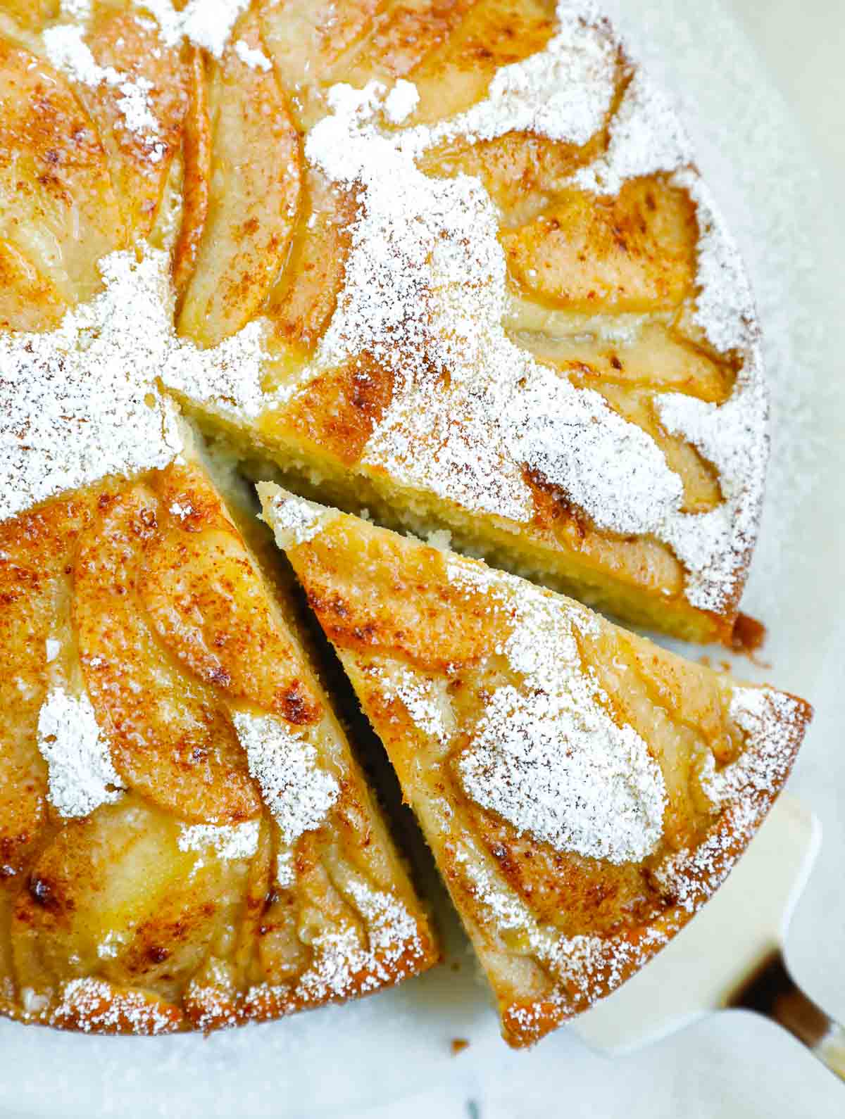 A piece of cake being taken out of the whole pear cake.