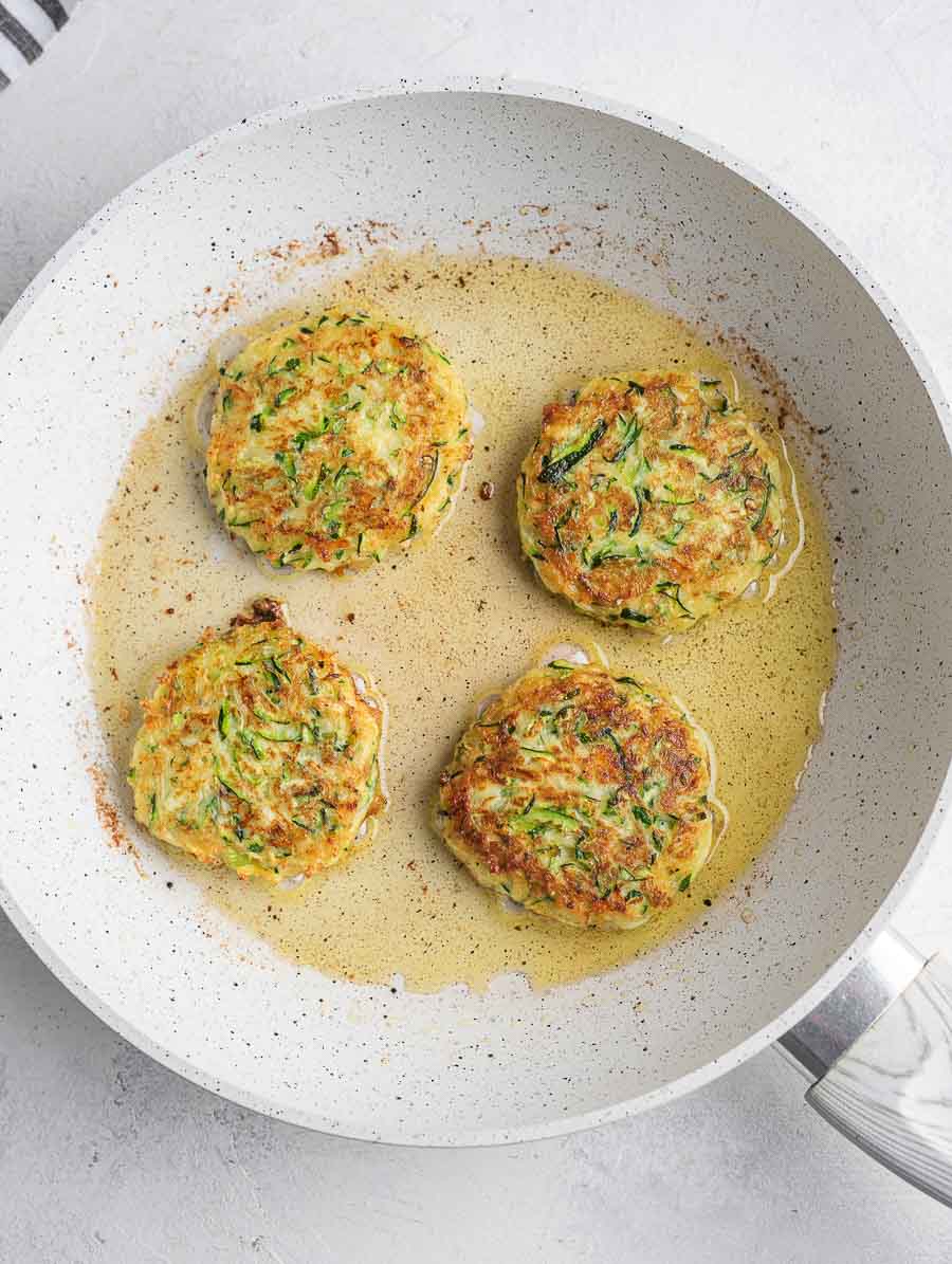zucchini fritters being fried in a pan