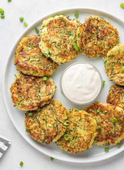 zucchini fritters on a white plate with dipping sauce