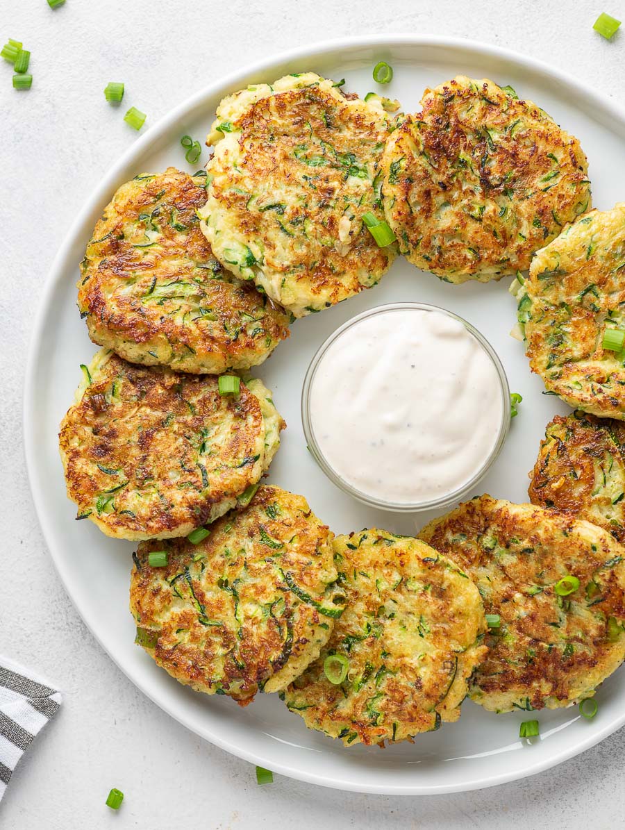 zucchini fritters on a white plate with dipping sauce