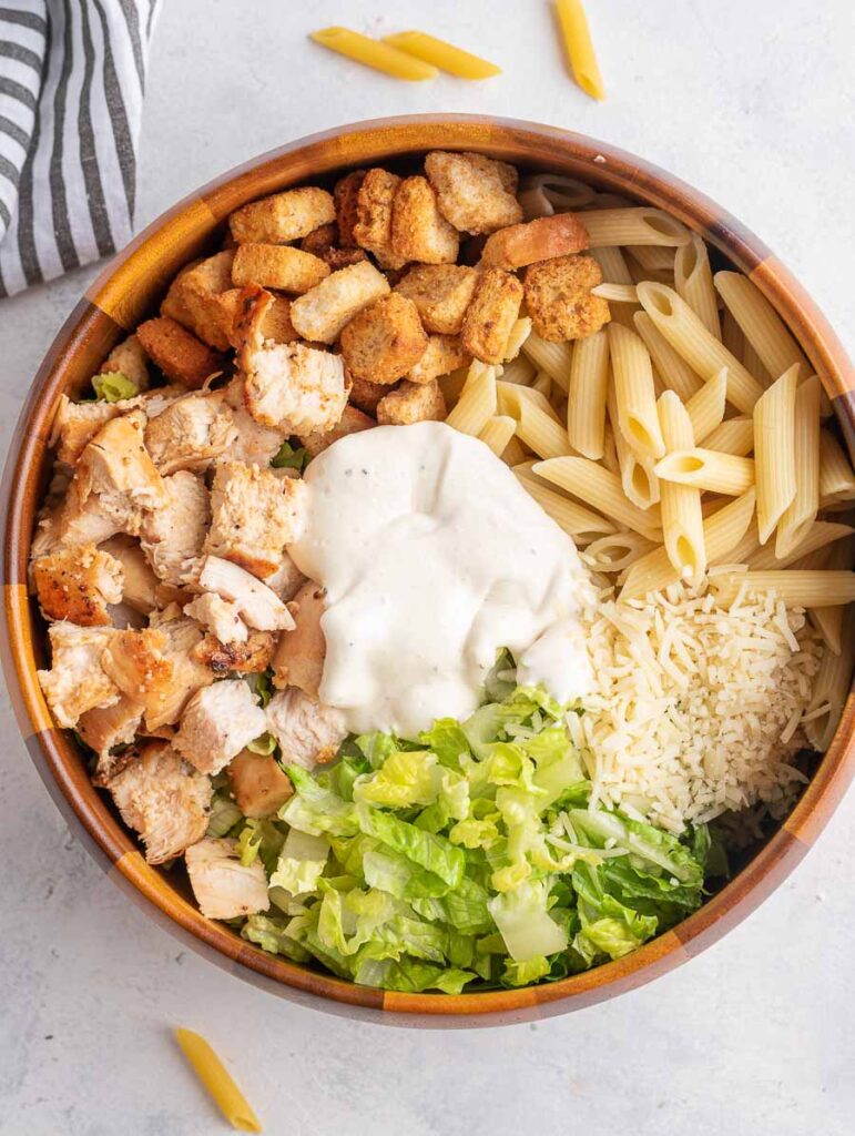 ingredients of chicken ceasar pasta salad in a wooden bowl