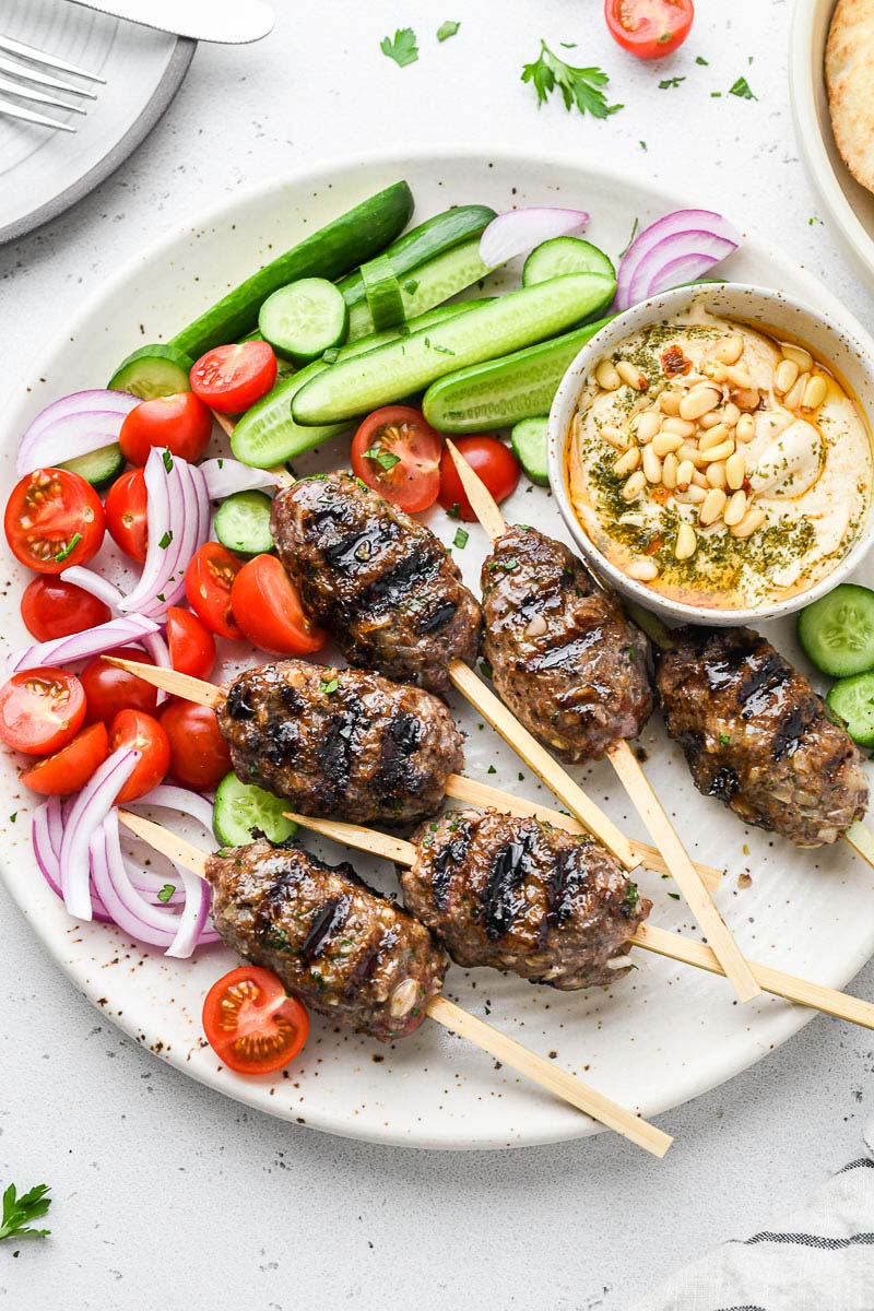 beef kofta skewers on a plate with veggies and hummus