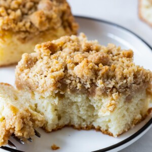 a piece of apple crumb cake on a plate with a bite taken out of it.