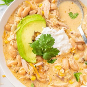 white chicken chili recipe on a white plate, topped with sour cream and avocado