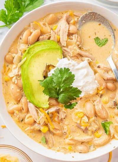 white chicken chili recipe on a white plate, topped with sour cream and avocado