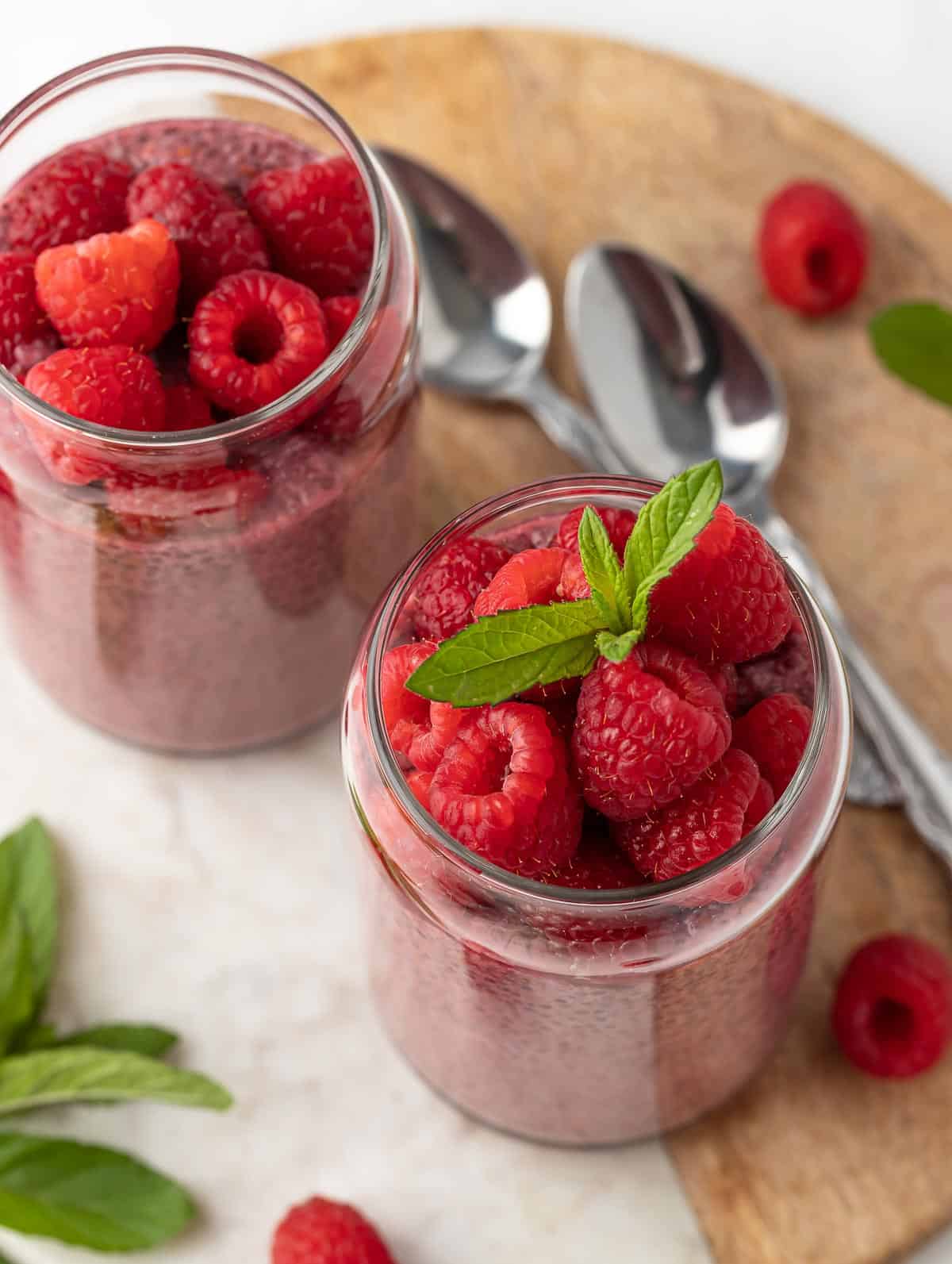 top shot of Raspberry Protein Chia Seed Pudding, topped with fresh raspberry and mint leaf on top and two spoons on the side