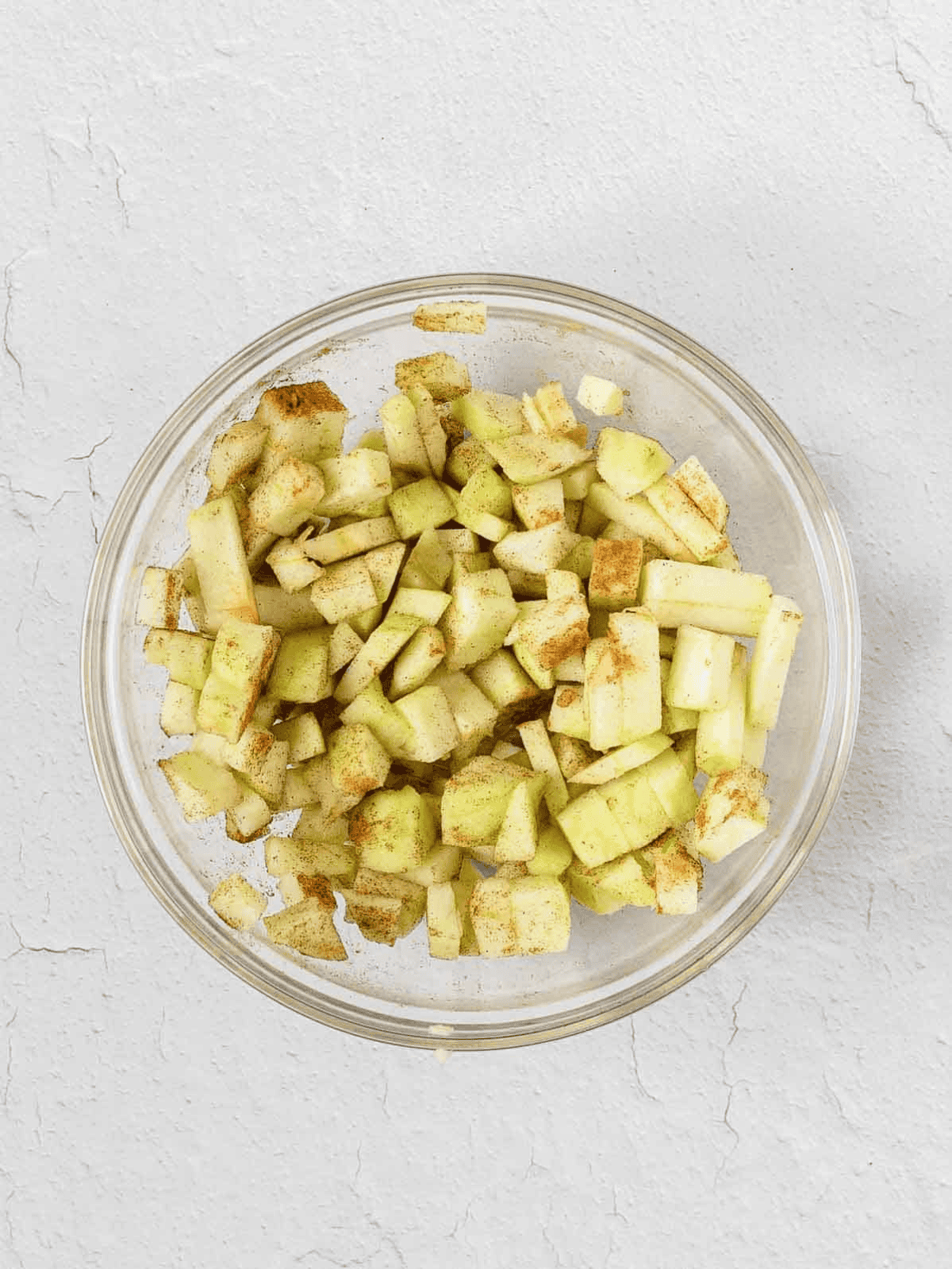 Diced apples tossed with ground cinnamon in a glass bowl.