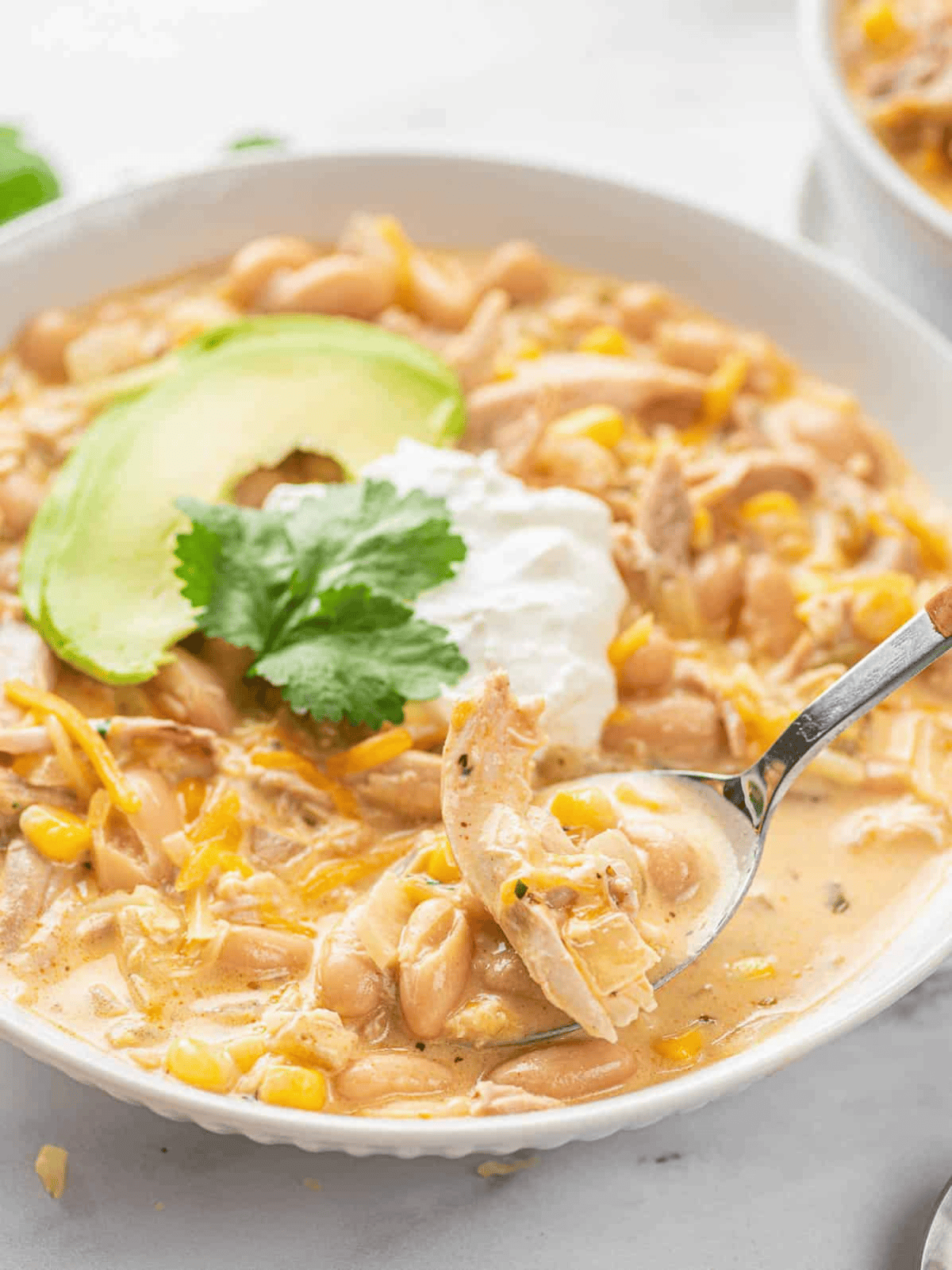 White chicken chili served in a bowl with avocao slices and sour cream on top.