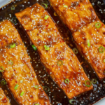Baked teriyaki salmon fillets topped with sesame seeds and sliced green onions.
