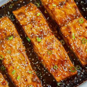 Baked teriyaki salmon fillets topped with sesame seeds and sliced green onions.