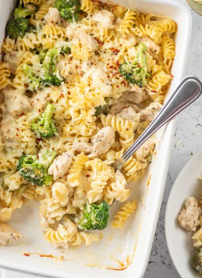 baked chicken and broccoli pasta in a white dish after baking with a spoon inside the dish