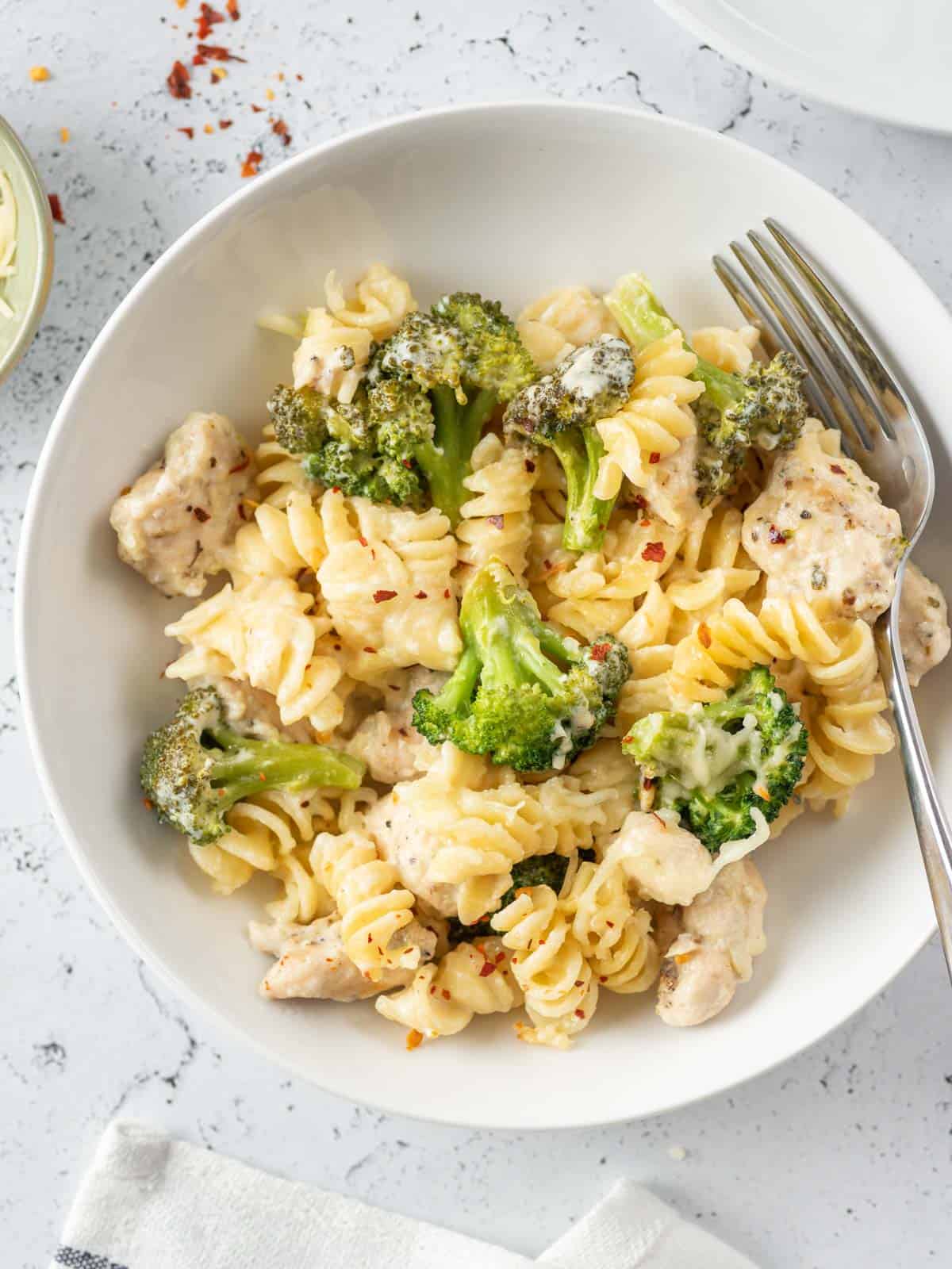 a fork paid on the side of the pasta and broccoli dish on a plate