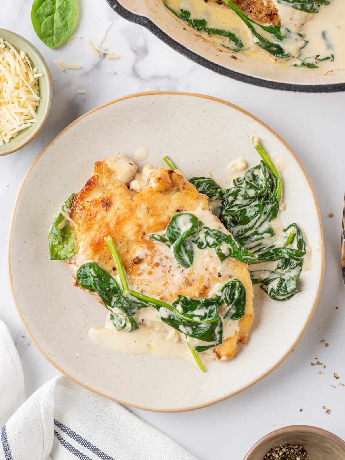 piece of creamy chicken florentine on a plate with cooked spinach leaves