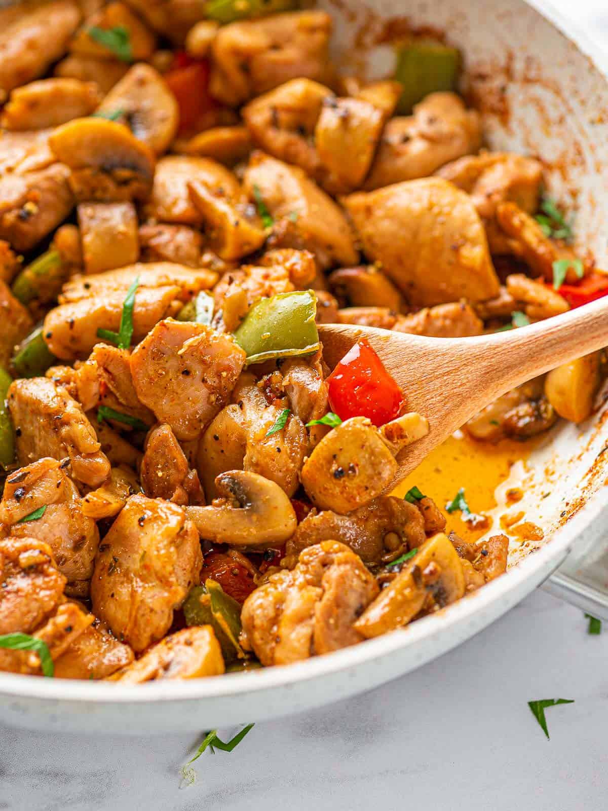 A pan of Garlic Mushroom Chicken Bites with a wooden spoon inside.