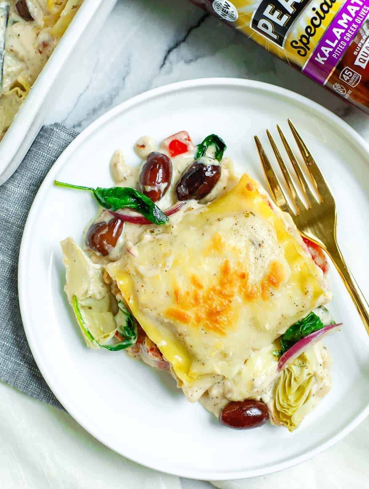 Piece of Greek White Alfredo Lasagna Roll on a plate with a gold fork