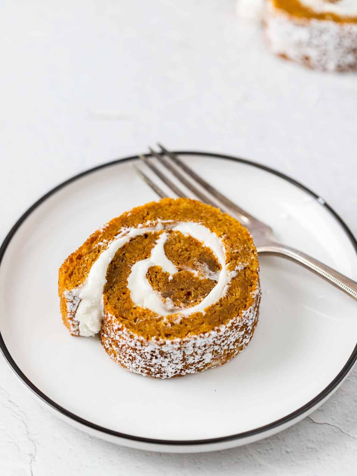 a slice of pumpkin cake roll on a plate with a fork