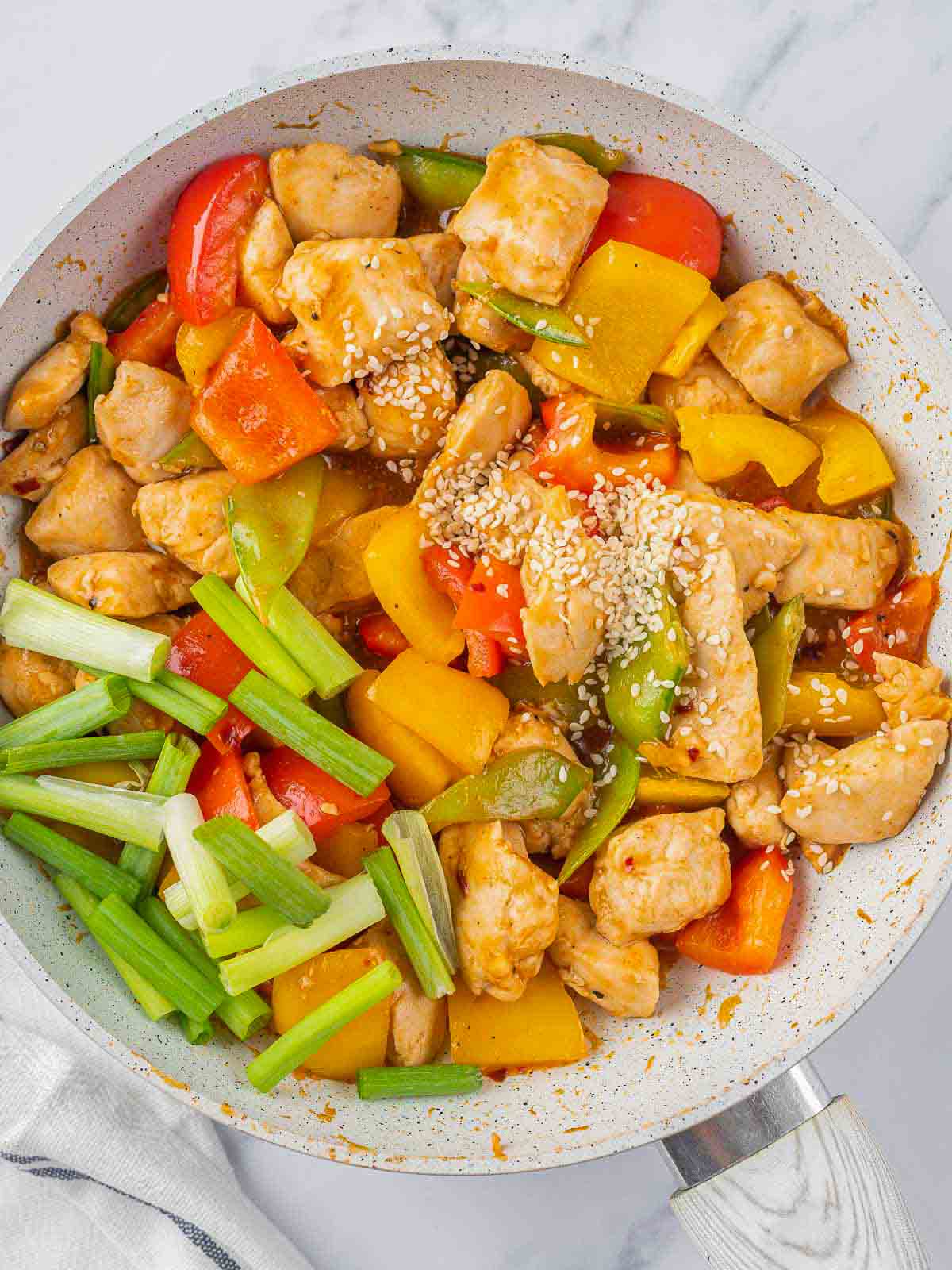 Sesame seeds and green onions added to a pan.