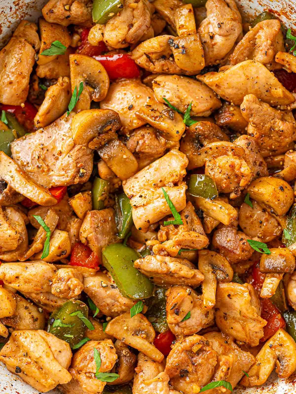 Close-up of chicken bites with mushrooms and red and green bell peppers.