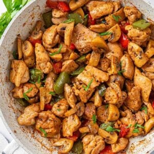 Chicken pieces with sautéed mushrooms, red and green bell peppers, and parsley in a skillet.