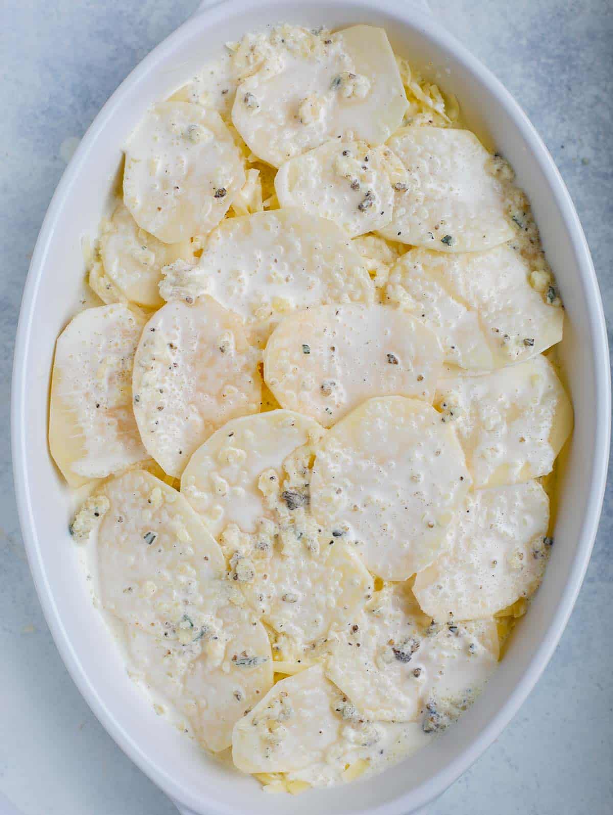 Top down shot of the au gratin potatoes in a white dish before baking