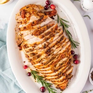 overhead shot of sliced turkey breast on a white plate with cranberry and rosemary stalks