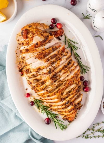 overhead shot of sliced turkey breast on a white plate with cranberry and rosemary stalks