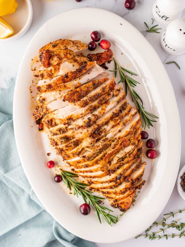 overhead shot of sliced turkey breast on a white plate with cranberry and rosemary stalks